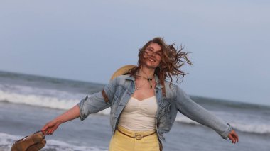  Kot ceketli neşeli genç bir kadın. Kolları açık. Okyanusun ve yaz akşamının tadını çıkarıyor.