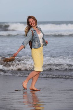 Sırt çantalı neşeli, orta yaşlı bir kadın sahilde yürüyor.