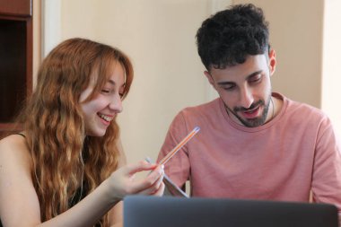 Genç ve neşeli çift evde dizüstü bilgisayar kullanarak ders çalışıyor.