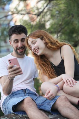 Gülümseyen genç çift dışarıda akıllı telefon kullanıyor.