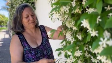 Yaşlı Latin Guarani kadın bahçe işleri arka bahçesinde yasemin bitkisiyle ilgileniyor.