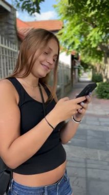 Oldukça neşeli bir genç kız. Yaz günü sokakta cep telefonu kullanıyor. Mesajlaşıyor ve konuşuyor.