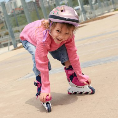 Şehir parkında paten giyen neşeli küçük kız.
