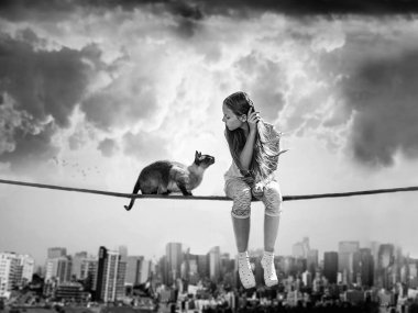 A little girl sitting on a rope with cat above a cityscape . Concept of childhood imagination, dream, freedom and happiness. clipart