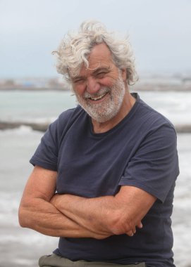 Arka planda okyanusla gülümseyen yaşlı bir adamın portresi.