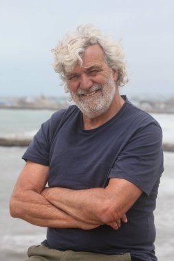 Arka planda okyanusla gülümseyen yaşlı bir adamın portresi.