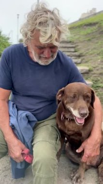 Yaşlı adam parkta merdivenlerde oturan köpeğiyle bağ kuruyor.