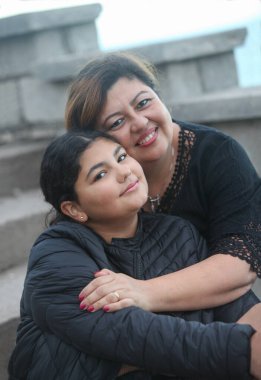 Genç kızını kucaklayan mutlu İspanyol annenin portresi. Bulutlu bir sonbahar gününde açık havada 