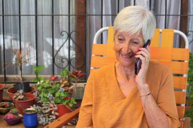 Bahçesinde oturan akıllı telefonu kullanan neşeli, son sınıf öğrencisi kadın.