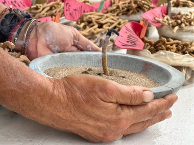 Sokak pazarındaki el yapımı tütsü çubuklarının yakın çekimi. Elinde yanan tütsü çubuğu olan bir satıcının elleri var.