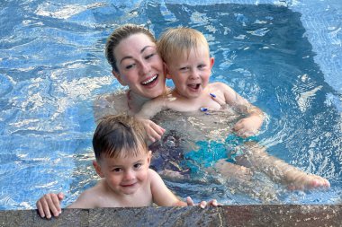 Mutlu anne ve küçük çocukları havuzda yüzüyorlar.