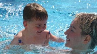 Anne ve küçük oğlu yüzme havuzunda. Çalıyor ve gülüyor