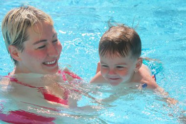 Anne ve küçük oğlu yüzme havuzunda. Çalıyor ve gülüyor