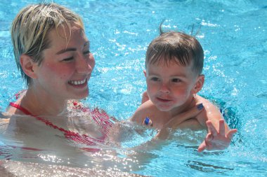 Anne ve küçük oğlu yüzme havuzunda. Çalıyor ve gülüyor