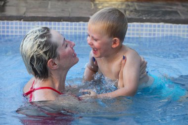 Anne ve küçük oğlu yüzme havuzunda. Çalıyor ve gülüyor