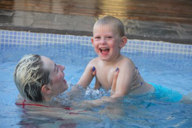 Anne ve küçük oğlu yüzme havuzunda. Çalıyor ve gülüyor