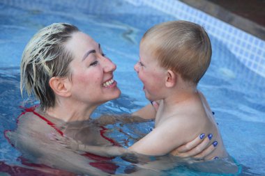 Anne ve küçük oğlu yüzme havuzunda. Çalıyor ve gülüyor