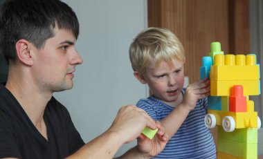Baba ve yeni yürümeye başlayan oğlu evde plastik yapı taşlarıyla oynuyorlar ve yaratıcı öğrenim