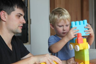 Baba ve yeni yürümeye başlayan oğlu evde plastik yapı taşlarıyla oynuyorlar ve yaratıcı öğrenim