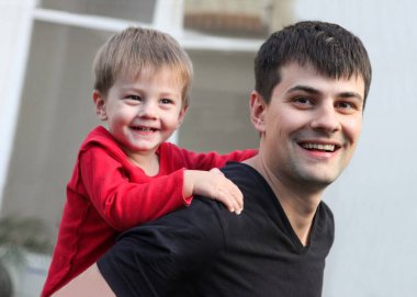 Neşeli bir babanın portresi küçük oğlunu omuzlarında taşırken eğleniyor.