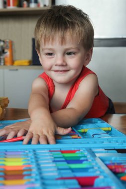  Evde çizim setiyle oynayan küçük çocuk renkli kalem ve kalemlere bakıyor.