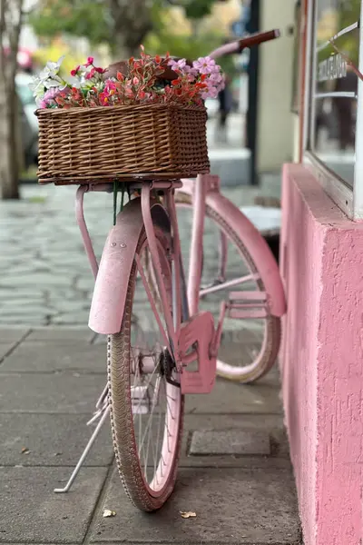 Pembeye boyanmış ve açık hava dekorasyonu olarak yeniden tasarlanmış eski bir bisiklet renkli çiçeklerle dolu sepetlerle dolu bir evin girişinde duruyor. Geri dönüşüm ve yaratıcılık.