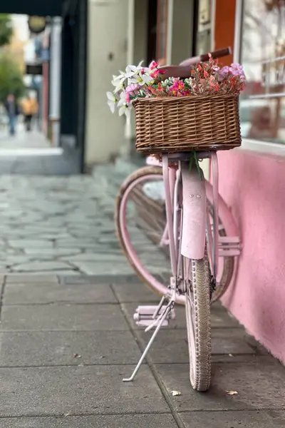 Pembeye boyanmış ve açık hava dekorasyonu olarak yeniden tasarlanmış eski bir bisiklet renkli çiçeklerle dolu sepetlerle dolu bir evin girişinde duruyor. Geri dönüşüm ve yaratıcılık.