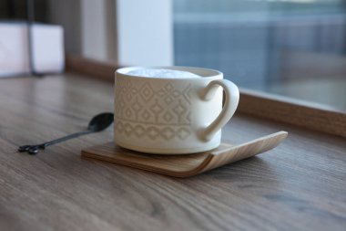 Bir fincan kahve ya da çay, cam kenarında çay kaşığı, yumuşak doğal ışık ve sıcak atmosfer.