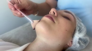 Güzellik kliniğinde ya da kaplıcada yüz bakımı sırasında genç bir kadının yüzüne yaklaş. Güzellik uzmanı yağ ya da maskeyi fırçayla sürüyor..