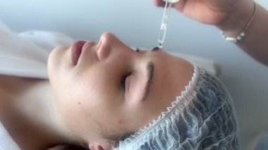 Güzellik merkezi ya da estetik kliniğinde cilt bakımı gören bir kadın, güzellik uzmanının yüz yağı ya da serum sürmesiyle...