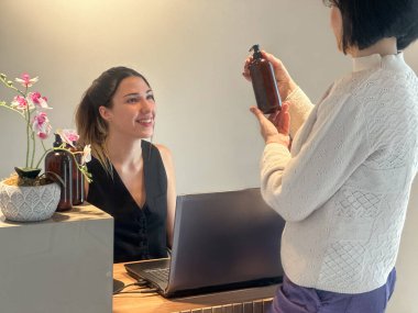 Spa ya da güzellik salonunda müşteriyle konuşan genç bir resepsiyonist. Masada losyon şişeleri var..