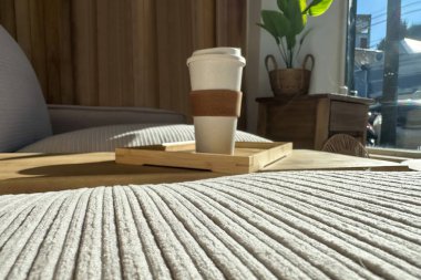 Pastel kumaşlı rahat bir kanepe, inşa masasında bir kahve fincanı, pencereden süzülen doğal güneş ışığı, ve ahşap ışıklı duvarlar, sakin, dünyevi ve rahat bir atmosfer yaratıyor.