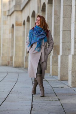 Kızıl saçlı kadın, 30 'larında, şehirde yürüyor, palto ve eşarp giyiyor. Sonbahar ya da bahar modası, mutlu ve şık..