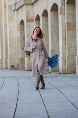 Kızıl saçlı kadın, 30 'larında, şehirde yürüyor, palto ve eşarp giyiyor. Sonbahar ya da bahar modası, mutlu ve şık..