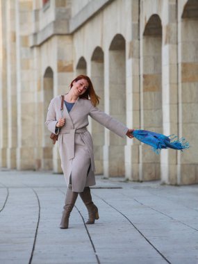 Kızıl saçlı kadın, 30 'larında, şehirde yürüyor, palto ve eşarp giyiyor. Sonbahar ya da bahar modası, mutlu ve şık..