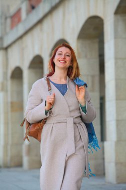 Kızıl saçlı kadın, 30 'larında, şehirde yürüyor, palto ve eşarp giyiyor. Sonbahar ya da bahar modası, mutlu ve şık..