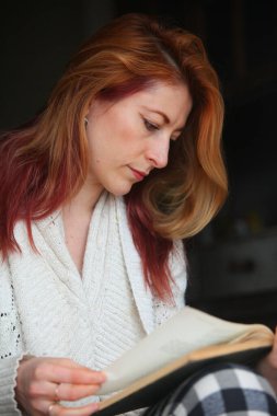 Kızıl saçlı kadın, 30 'lu yaşlarda, terasta rahat ev elbiseleriyle oturuyor, kitap okuyor. Doğal ışık, bahar ya da sonbahar havasında huzurlu ve rahat bir an..