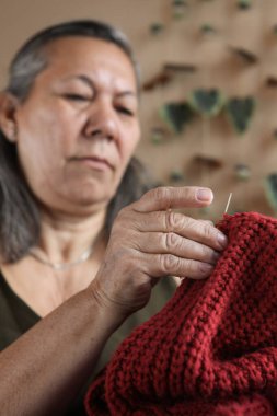 Elle örülmüş bir süveteri onaran yaşlı Latin kadın, rahat bir ortamda sanatına odaklanmış..