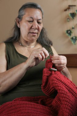 Elle örülmüş bir süveteri onaran yaşlı Latin kadın, rahat bir ortamda sanatına odaklanmış..