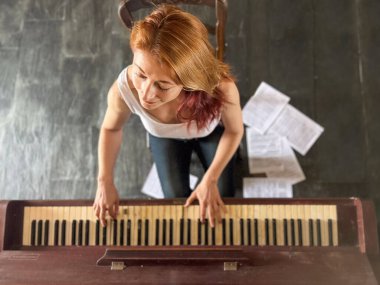Kızıl saçlı kadın, 30 'larında, evde eski bir piyano çalıyor. Yüksek açılı görüntüsü ve yerde notaları var..