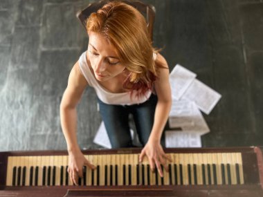 Kızıl saçlı kadın, 30 'larında, evde eski bir piyano çalıyor. Yüksek açılı görüntüsü ve yerde notaları var..