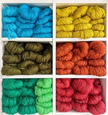 Temiz beyaz raflarda çeşitli renklerde yün, yün ve pamuk ipliklerinden oluşan canlı bir karışım.