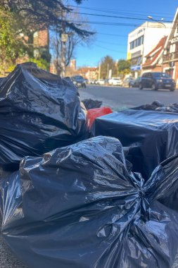 Şehir caddesinde kaldırımda arka planda sokak olan siyah çöp torbalarına yakın çekim.. 
