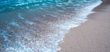 Beyaz kumlu bir kumsalın arka planı ve gün boyunca sevimli küçük dalgalar.