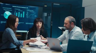 Modern ofis toplantı odasında çeşitli iş adamları strateji tartışıyor ve dijital ekranda verileri analiz ediyor. Şirket takım çalışması, planlama ve işbirliği kavramı.