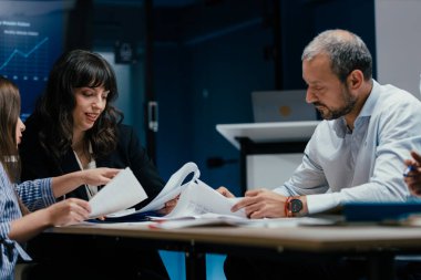 Üst düzey yöneticiler ve asistanlar lüks bir C-suit yönetim kurulunda önemli bir performans değerlendirme toplantısı düzenlerler. Farklı yaşlardan beyaz profesyoneller masa etrafında kağıt ve dizüstü bilgisayarlarla strateji tartışıyor.