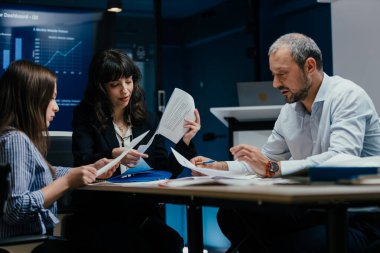 Üst düzey yöneticiler ve asistanlar lüks bir C-suit yönetim kurulunda önemli bir performans değerlendirme toplantısı düzenlerler. Farklı yaşlardan beyaz profesyoneller masa etrafında kağıt ve dizüstü bilgisayarlarla strateji tartışıyor.