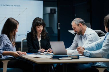 Üst düzey bir şirket yönetim kurulundaki yatırım riskini değerlendiren beyin fırtınası oturumunda aralarında yönetici ve asistanların da yer aldığı dört profesyonel işbirliği yapıyor. Stratejik toplantı, lüks ofis ortamında takım çalışması ve analizleri gösteriyor..