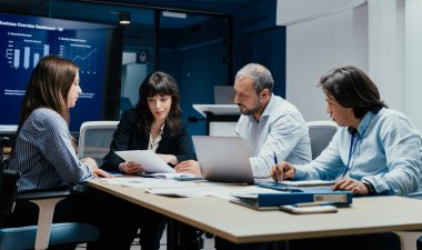 Üst düzey bir şirket yönetim kurulundaki yatırım riskini değerlendiren beyin fırtınası oturumunda aralarında yönetici ve asistanların da yer aldığı dört profesyonel işbirliği yapıyor. Stratejik toplantı, lüks ofis ortamında takım çalışması ve analizleri gösteriyor..