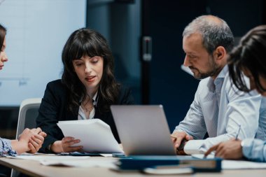 Üst düzey bir şirket yönetim kurulundaki yatırım riskini değerlendiren beyin fırtınası oturumunda aralarında yönetici ve asistanların da yer aldığı dört profesyonel işbirliği yapıyor. Stratejik toplantı, lüks ofis ortamında takım çalışması ve analizleri gösteriyor..